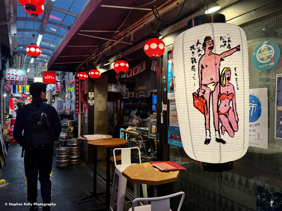 ถนนแคบ ๆ ของถนนสายลมโชคจิที่มีร้านค้าป้ายและคนเดินในช่วงเย็น